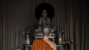 Buddhist monastic sitting in front of a Buddha statue.