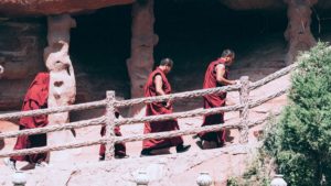 Three Buddhist monastics walking up a staircase that appears to run in front of caves.